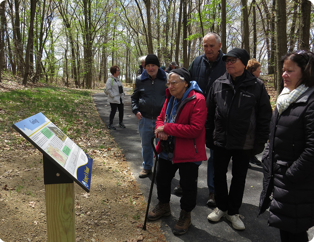 At a park, people are reading an informational plaque about one of the park's features